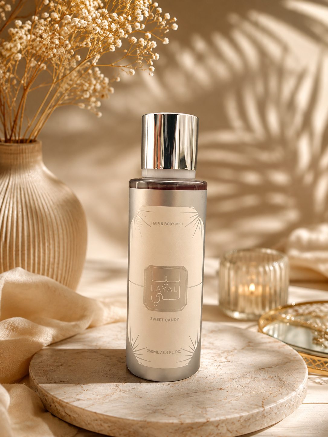 Flacon de brume parfumée Layal Sweet Candy 250 ml pour le corps et les cheveux, posé sur un plateau de marbre clair avec bougie et fleurs séchées