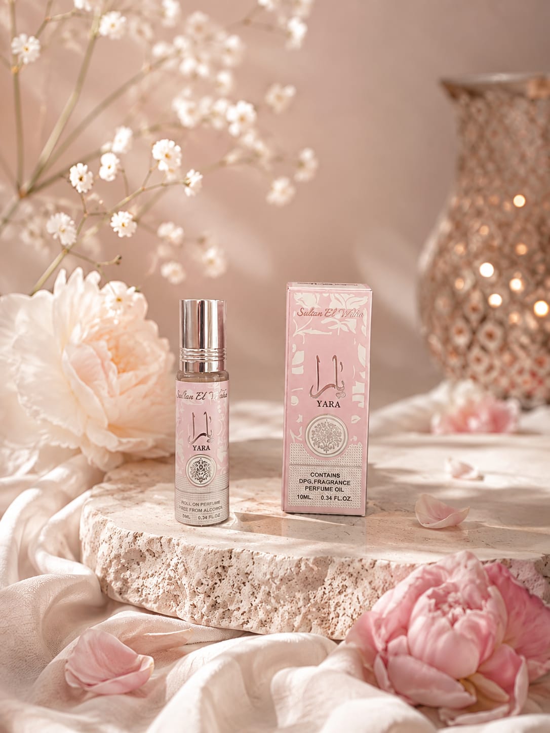 Huile de parfum Yara 10 ml gourmande et vanillée, flacon roll-on rose et son étui posés sur travertin, entourés de pivoines